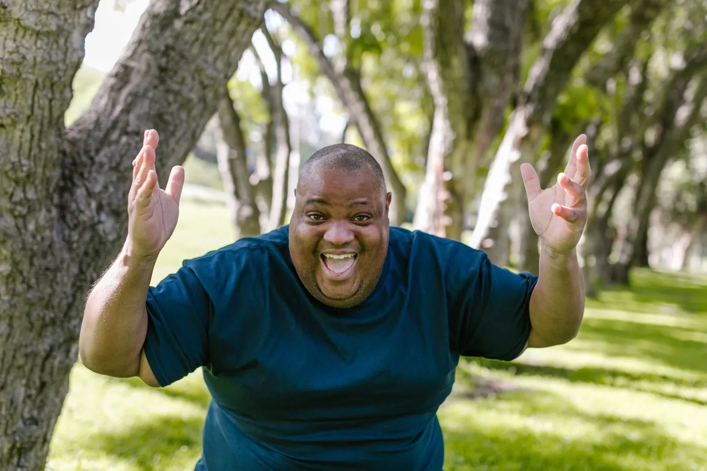 A man raising his arms joyfully in a sunny park