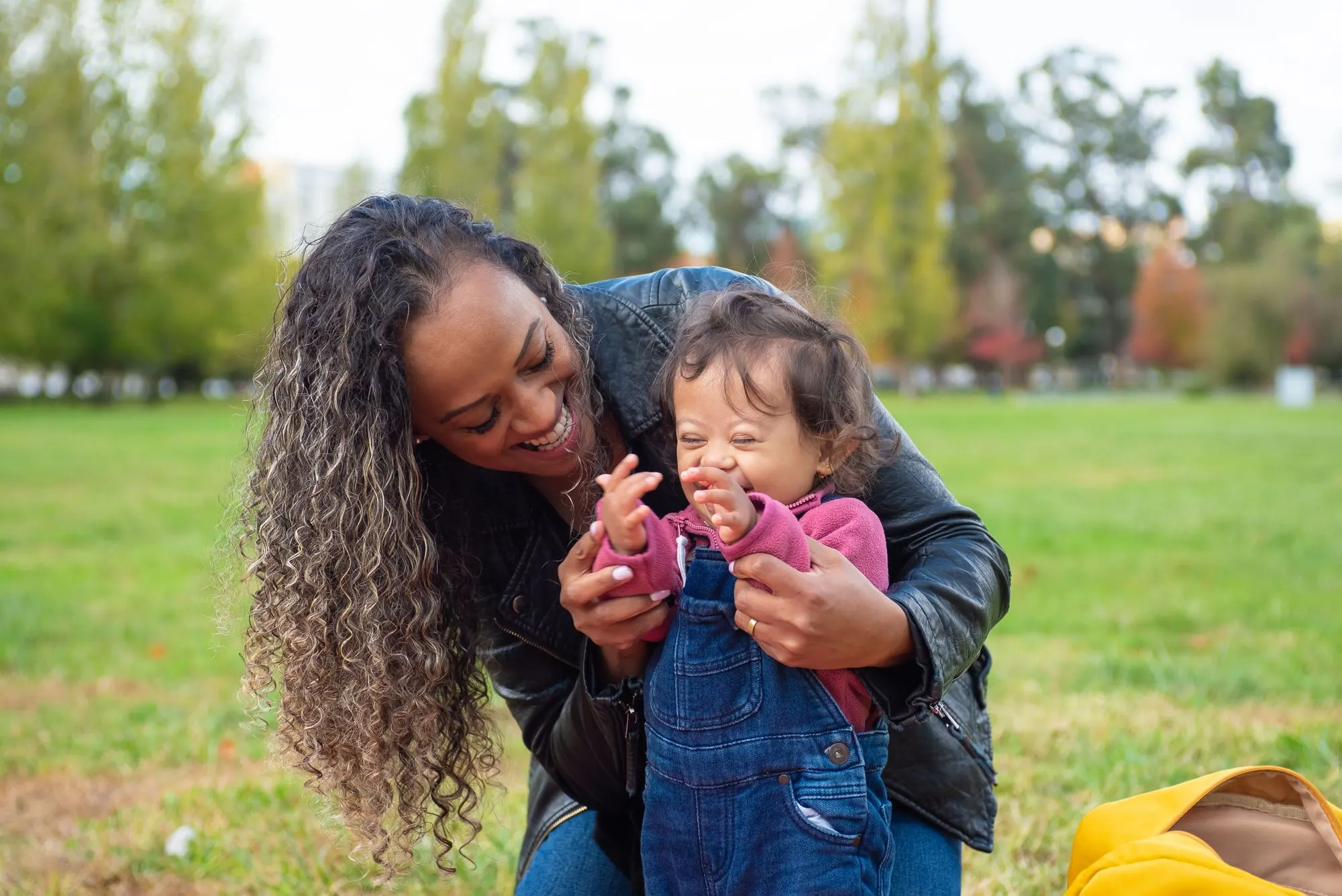 A mother laughing with her young child with Down syndrome in a park