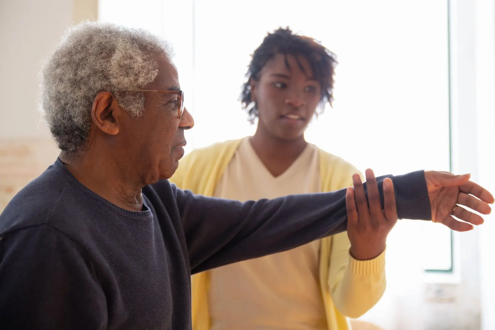 A caregiver helping an older man with arm exercises at home